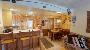 A compact kitchen with wooden cabinets, a dining area with a table and chairs, and a cozy seating area with a patterned sofa.