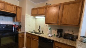 Cucina con mobili in legno, piano cottura nero, lavastoviglie, forno a microonde e ripiano in granito.