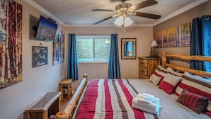 A bedroom with a large bed, wooden headboard, a ceiling fan, a window with curtains, and artwork on the walls. - Sugar Ski Premium Two Bedroom - Unit 821 (Sugar Mountain)