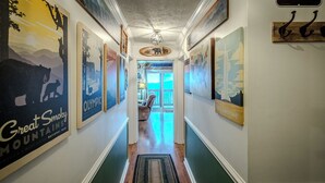 A hallway with framed posters of Yellowstone and Olympic National Parks, wooden floor, and a view into a room with a window. - Sugar Ski Premium Two Bedroom - Unit 821 (Sugar Mountain)
