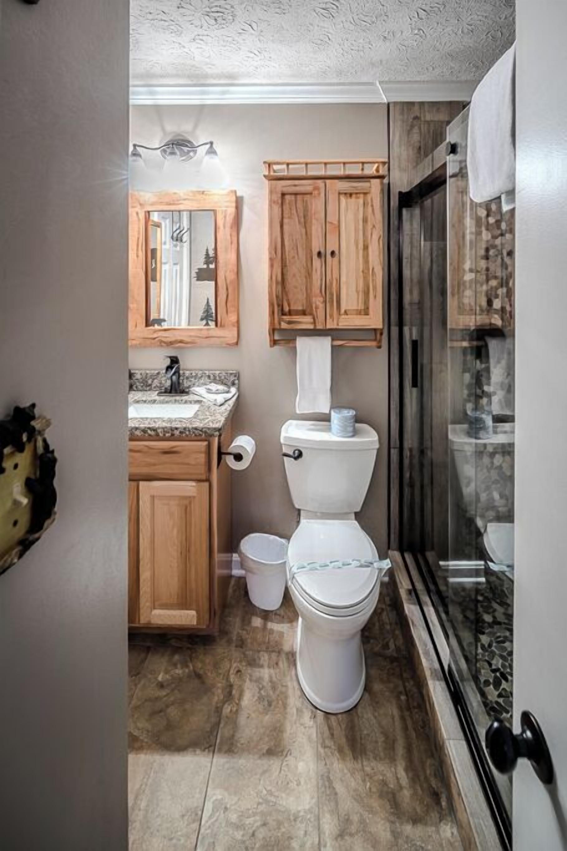 A compact bathroom with a toilet, wooden cabinets, a mirror, and a shower area.