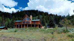 A large log cabin with a stone chimney, surrounded by a forest and a clear sky. - 29 Valley of the Pines with Hot Tub in the Upper Valley (Red River)