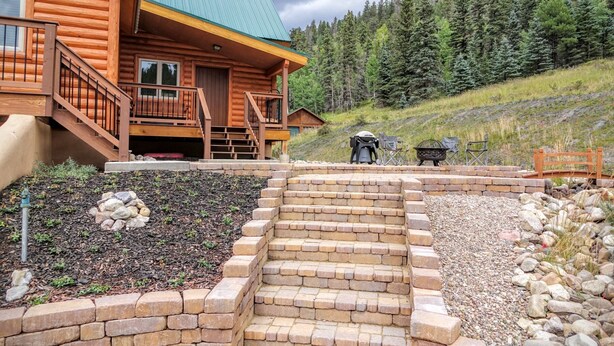 A log cabin with a green roof, a wooden deck, and a stone staircase leading to a patio area with outdoor seating and a grill. - 29 Valley of the Pines with Hot Tub in the Upper Valley (Red River)