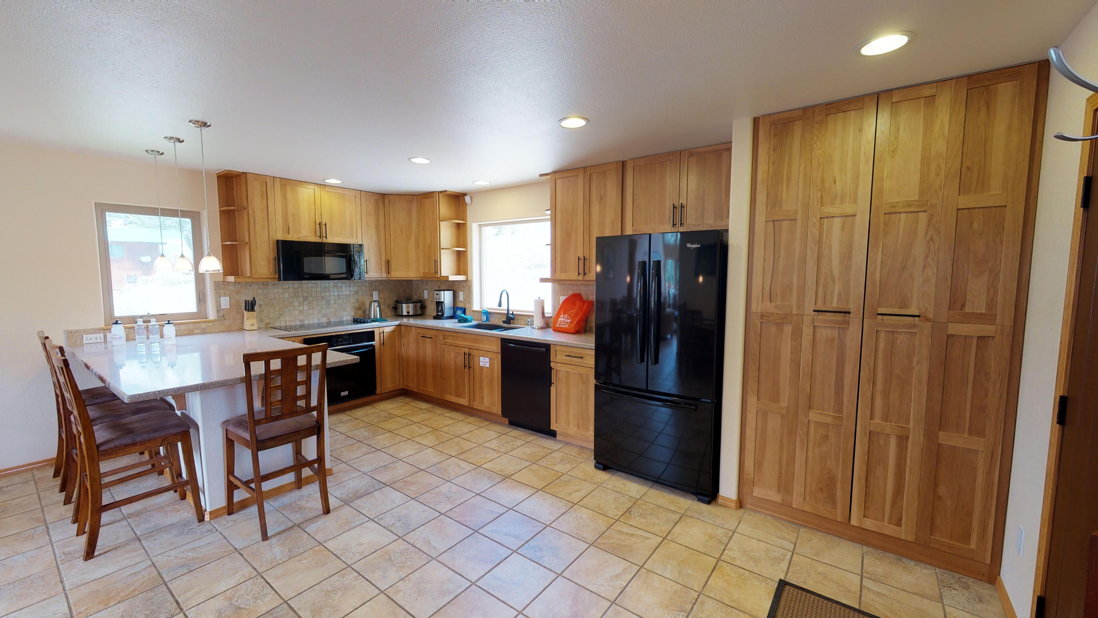 A spacious kitchen with wooden cabinets, a black refrigerator, and a central island with chairs.