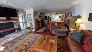 A cozy living room with a fireplace, a wooden coffee table, a sofa, and a dining area with chairs and a table.