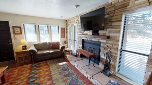A living room with a stone fireplace, a sofa, a television, and a patterned rug.