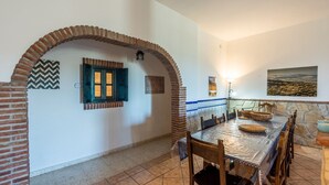 A dining area with a brick archway, a tiled wall with a blue and white pattern, a wooden table with chairs, and a stone wall with a painting. - Villa Fablas Periana by Ruralidays (Málaga)