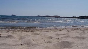 Una playa arenosa con olas suaves y una isla en la distancia.