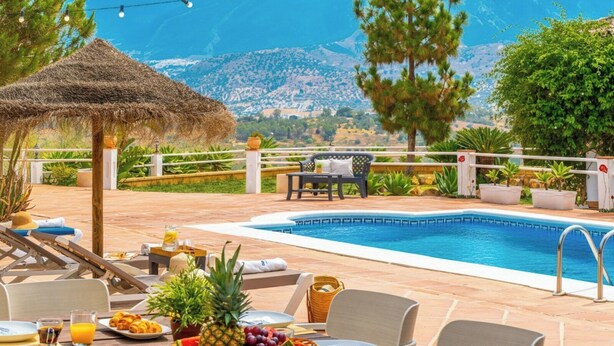 Un espace aménagé au bord de la piscine, avec un parasol en chaume, des chaises longues et une table à manger, ainsi que de l’assiette et des boissons.