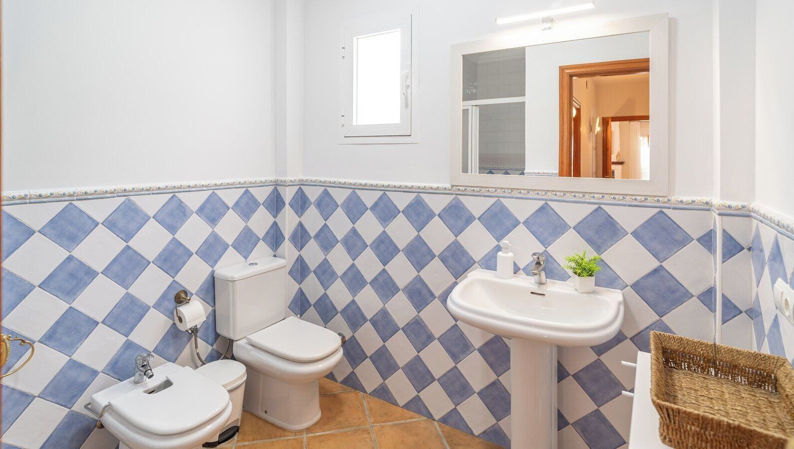 A bathroom with a blue and white checkered tile backsplash, a white sink, and two toilets.