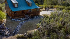 Une cabane en bois avec un toit bleu, un chemin de pierre menant à l’entrée et, au fond, un terrain de basket.