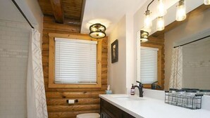Une salle de bain avec des murs en bois, des toilettes blanches, un lavabo avec un miroir et un espace douche.