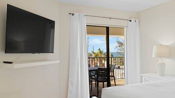 Une chambre d’hôtel avec un téléviseur fixé au mur, un balcon avec une table et des chaises, et une vue sur l’océan.