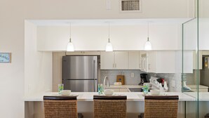 Una cocina moderna con un refrigerador de acero inoxidable, gabinetes blancos y una isla de vidrio con sillas de mimbre.