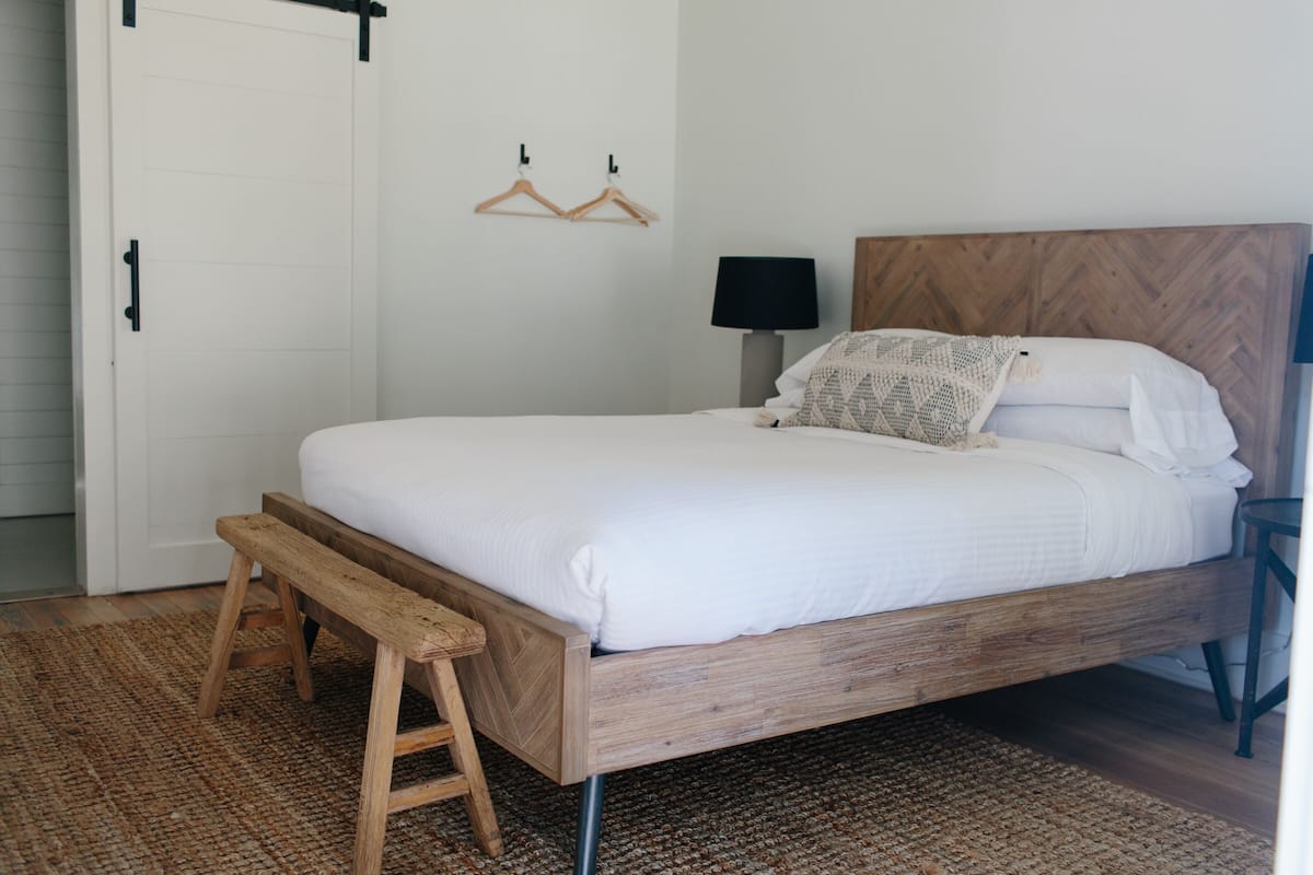 Ein Schlafzimmer mit einem hölzernen Bett, einer Bank, einer Wandlampe und einer Tür mit Griff.