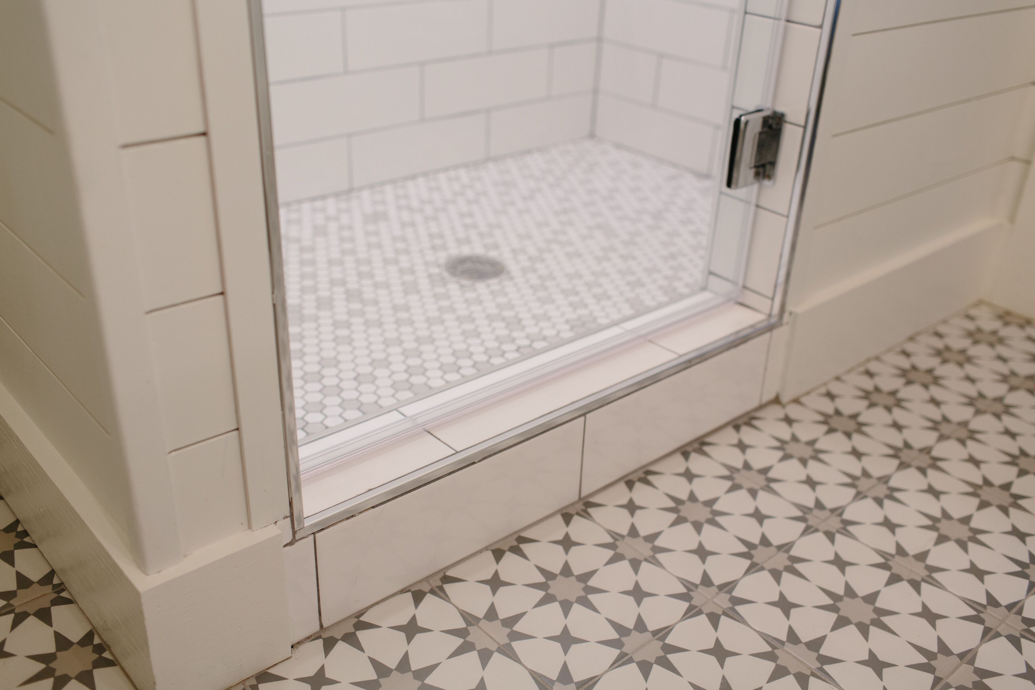 A shower area with a tiled floor and walls, a glass door, and a metal handle.