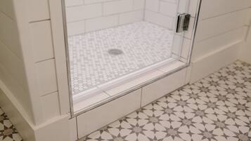 A shower area with a tiled floor and walls, a glass door, and a metal handle.