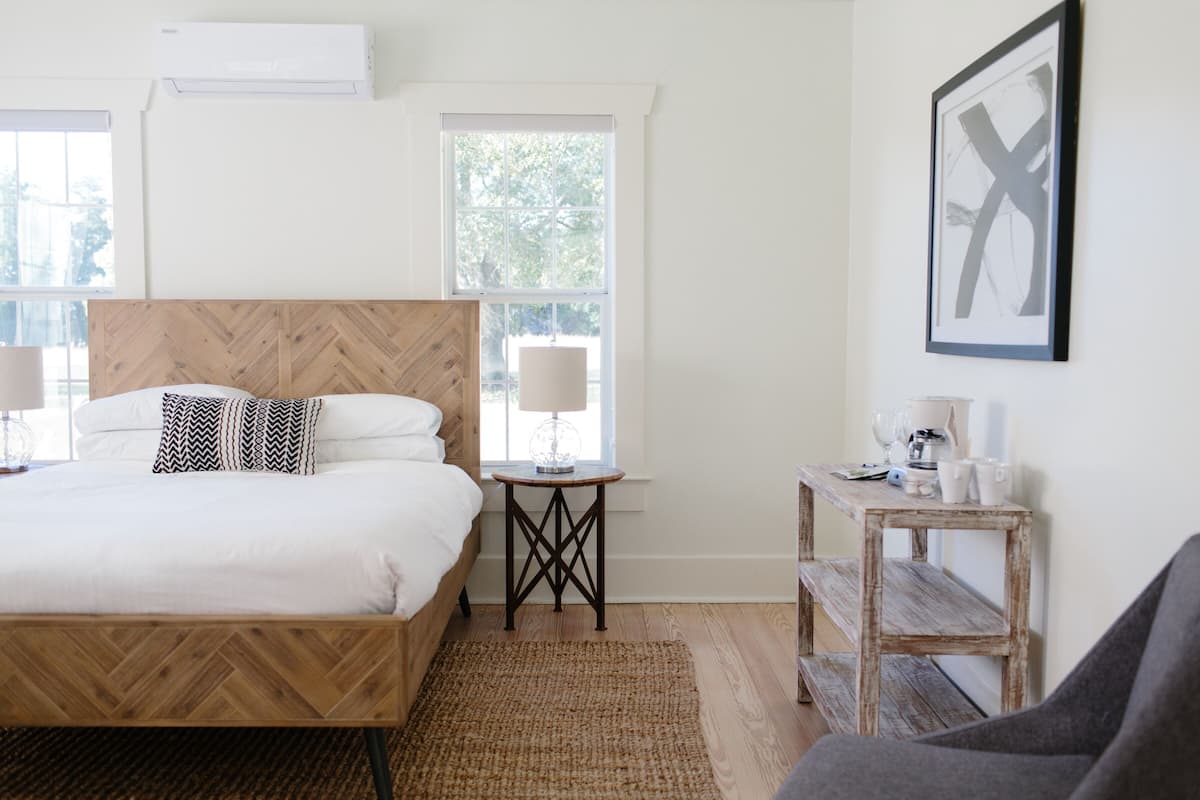 Ein Hotelzimmer mit einem hölzernen Bett, zwei Nachttischen, einer Bank und einer Wand-Klimaanlage.