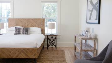A hotel room with a wooden bed, two bedside tables, a bench, and a wall-mounted air conditioner.