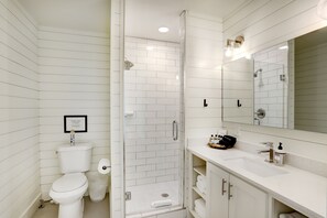 A modern bathroom with a toilet, a shower with a glass door, a sink, and a large mirror.