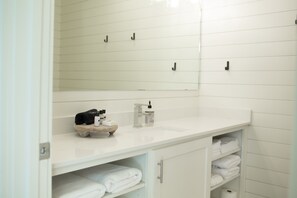 A bathroom with a white sink, mirror, and shelves with towels.