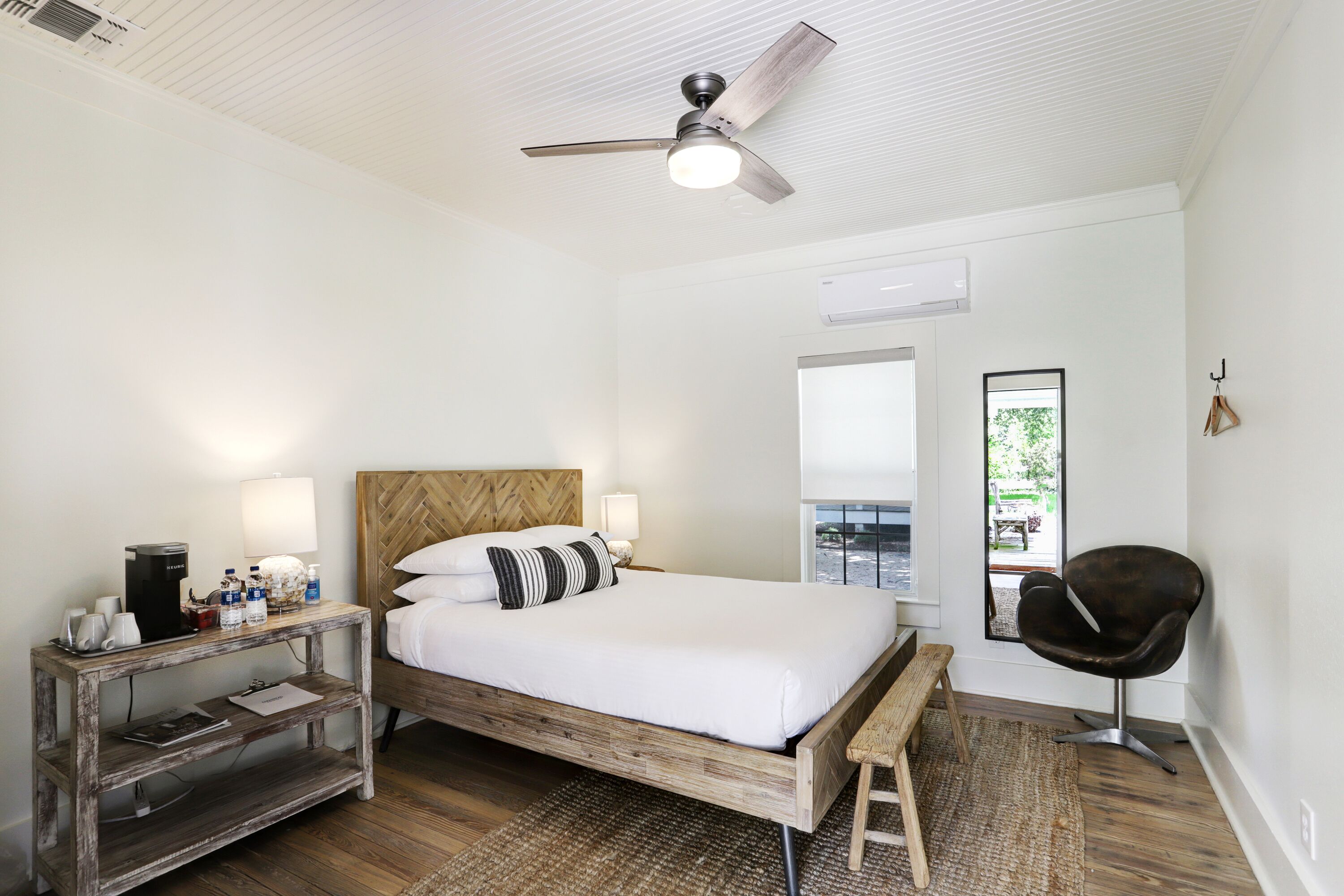 A modern bedroom with a wooden bed, bedside tables, a desk, a chair, and a ceiling fan.