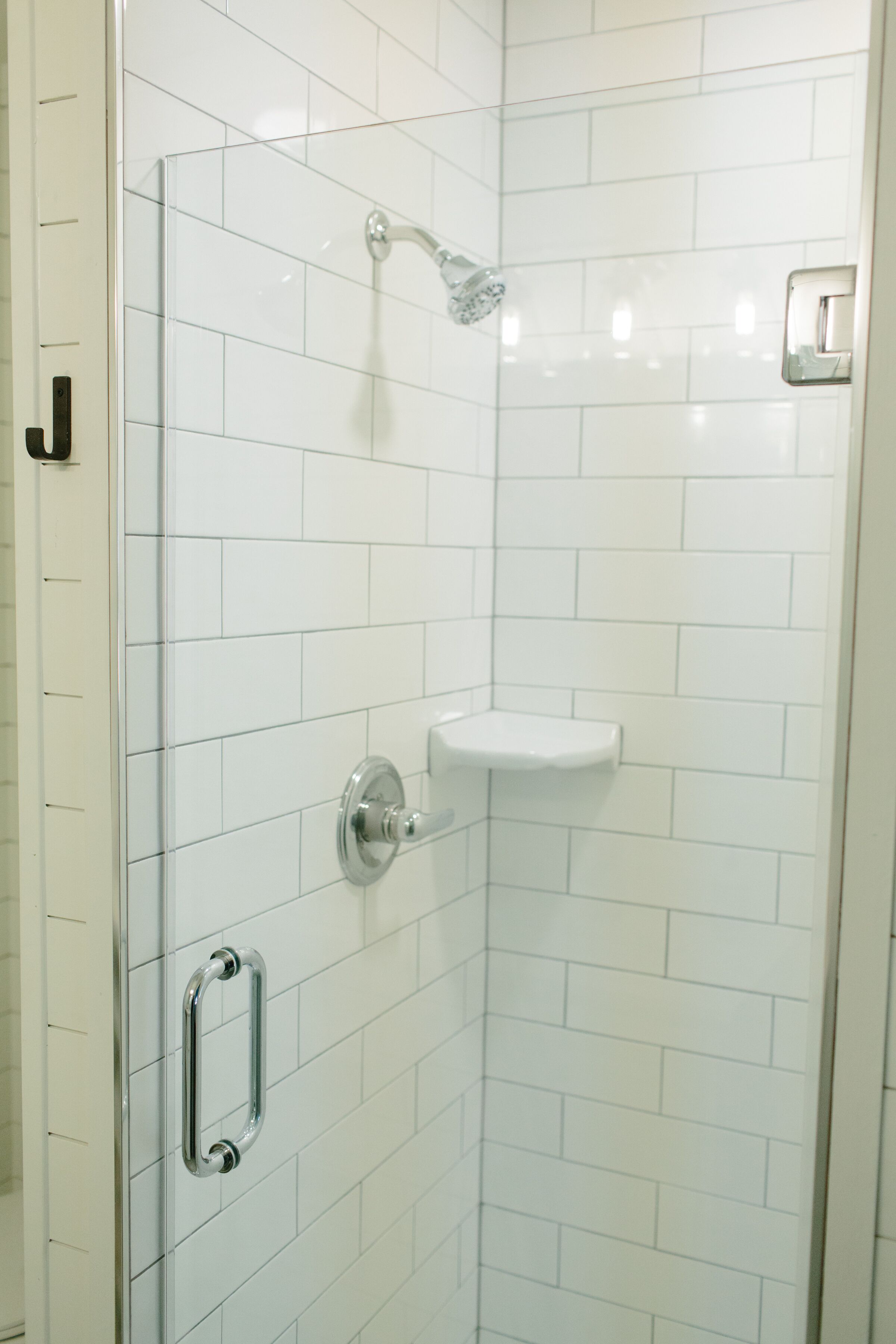 A glass-enclosed shower with a chrome showerhead and a white tiled wall.