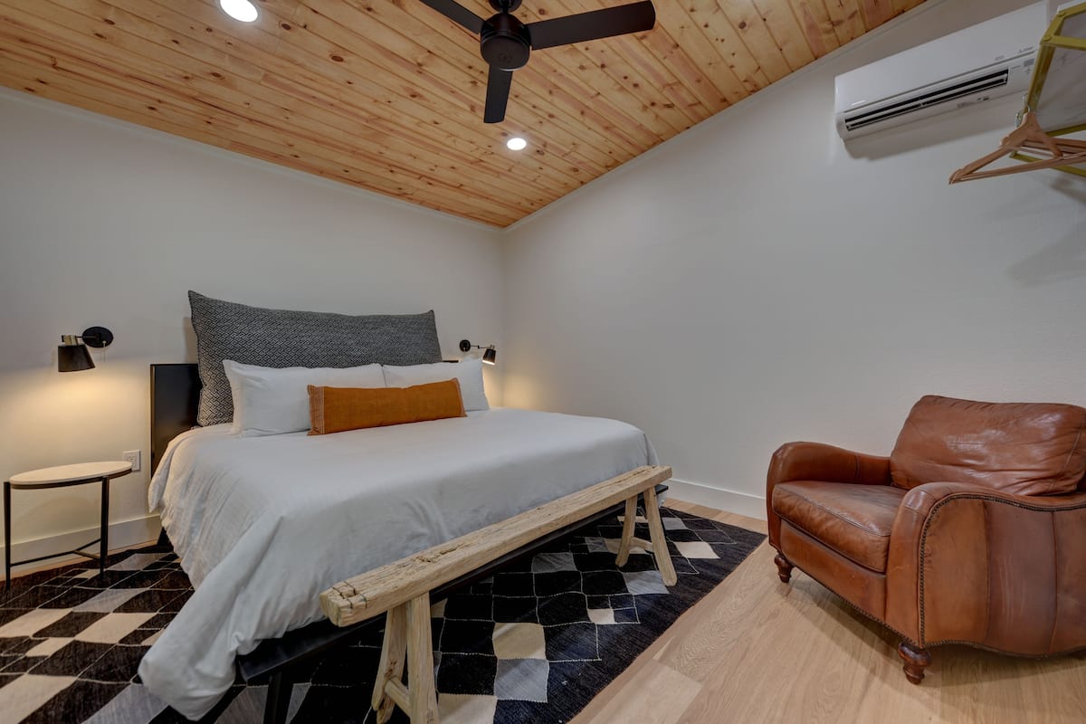 Ein Schlafzimmer mit einem Bett, einer Bank, einem braunen Ledersessel, einem kleinen Tisch und einem Deckenventilator.