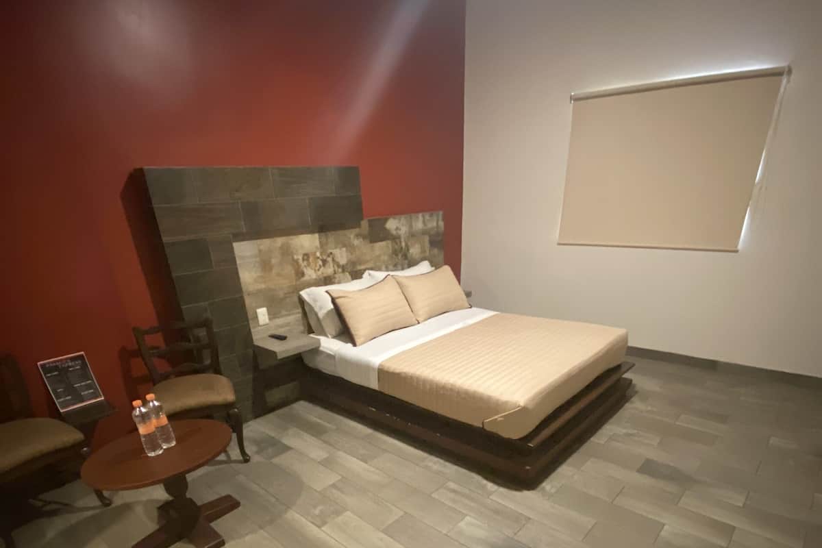 A modern bedroom with a large bed, a small table with bottles, a chair, and a stone accent wall.