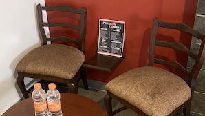 Una pequeña mesa redonda con dos sillas, cada una con un cojín. Hay dos botellas de agua sobre la mesa. Un letrero de menú está en la pared detrás de las sillas.