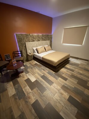 Un dormitorio moderno con una cama grande, suelo de madera y una pequeña mesa con sillas.