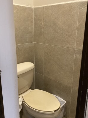 Une petite salle de bain fermée, équipée de toilettes et d’une poubelle.
