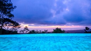 A swimming pool with a view of the sunset and surrounding trees.