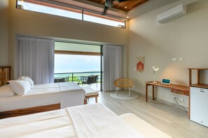 A hotel room with two beds, a desk, a chair, and a view of the sea.