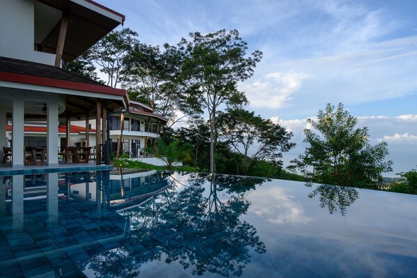 A modern resort with a infinity pool reflecting the surrounding trees and sky.