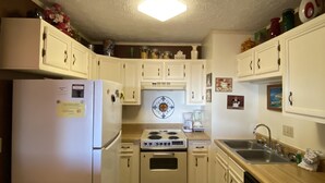 Une cuisine de taille réduite avec des meubles blancs, une cuisinière, un évier et un lave-vaisselle.