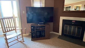 Un salon avec un téléviseur à écran plat posé sur un meuble en bois, une cheminée et un fauteuil à bascule.