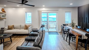 Ein modernes Wohnzimmer mit einer Couch, einem Esstisch mit Stühlen, einem Deckenventilator und Blick durch eine Glastür nach draußen.