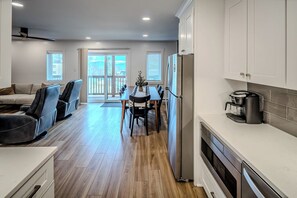 A modern kitchen with white cabinets, a dining area with a long table, and a view through the glass doors.