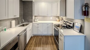 Eine moderne Küche mit weißen Schränken, einem Edelstahl-Geschirrspüler, einem eingebauten Backofen und einem kleinen Kühlschrank.