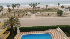 A view of a beach with palm trees, a parking lot, and a swimming pool. - Xeracsol I 5º, Solo Familias! (Xeraco Playa)
