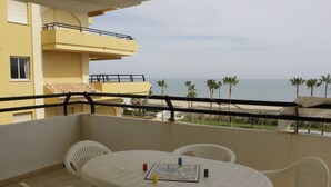 A balcony with a table and chairs, overlooking a beach with palm trees and the sea. - Xeracsol I 5º, Solo Familias! (Xeraco Playa)