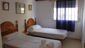 A hotel room with two single beds, wooden headboards, white linens, a window with blue curtains, and framed pictures on the wall. - Xeracsol I 5º, Solo Familias! (Xeraco Playa)