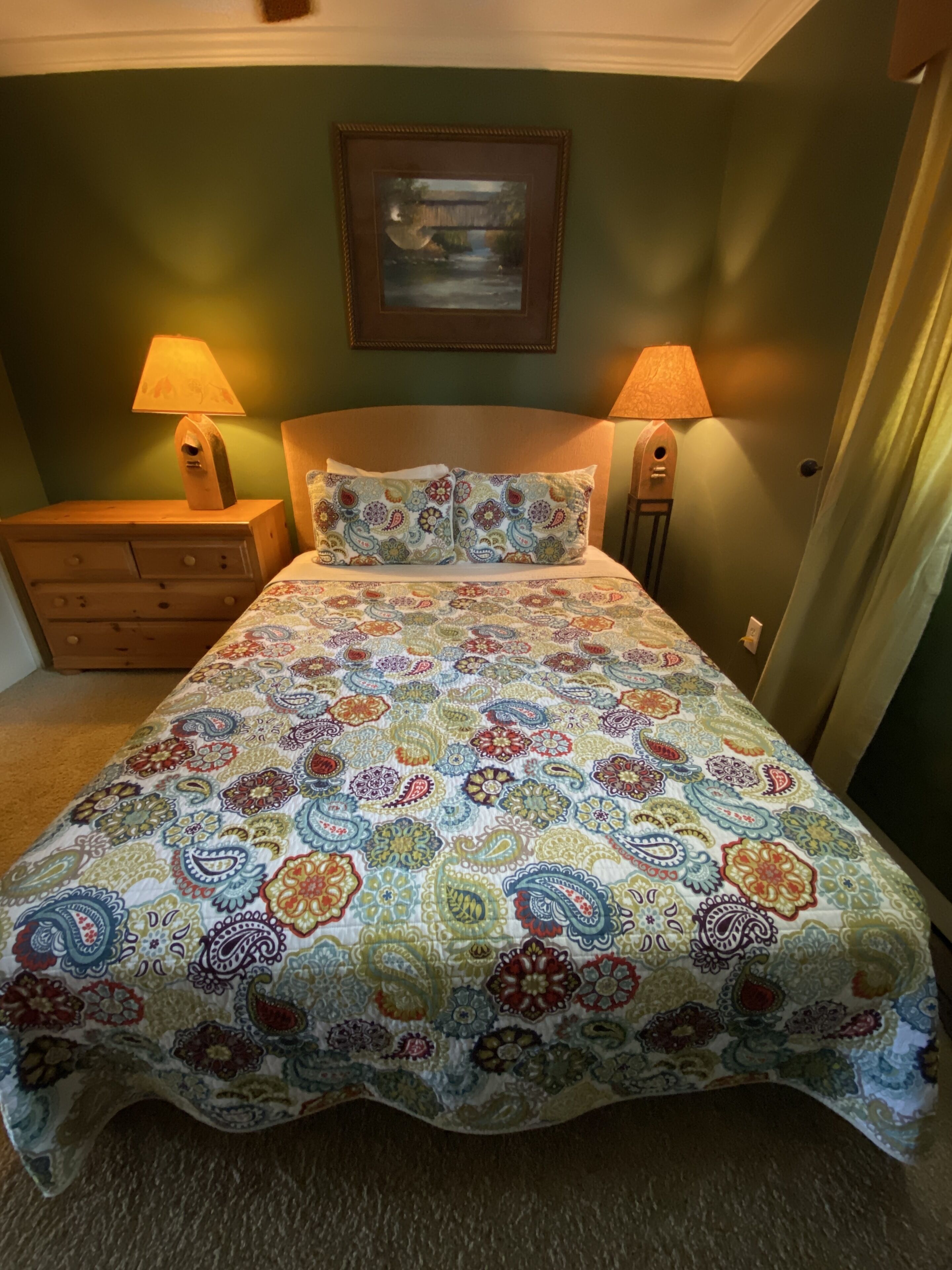 Ein Schlafzimmer mit einem gestreiften Bettbezug, zwei Nachttischlampen, einem Holznachttisch und einem gerahmten Bild an der Wand.