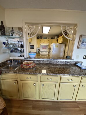 A kitchen with a granite countertop, a sink, and a refrigerator. There are cabinets with handles and a decorative mirror above the countertop.