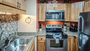 Uma cozinha moderna com armários de madeira, pia de aço inoxidável, micro-ondas, forno e geladeira.