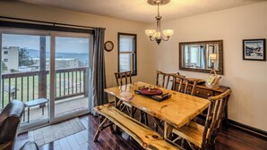 Comedor con mesa y sillas de madera, una araña de cristal y vistas a través de un ventanal corredera.