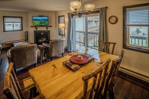 A dining area with a wooden table, chairs, a fireplace, a television, and a view of the outdoors.