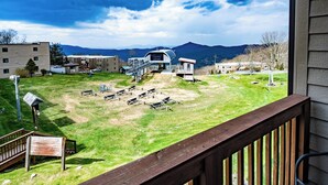 A residential area with a grassy yard, a wooden deck, and a view of mountains in the background.