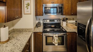A kitchen with wooden cabinets, a stainless steel microwave, a stove, and a refrigerator.